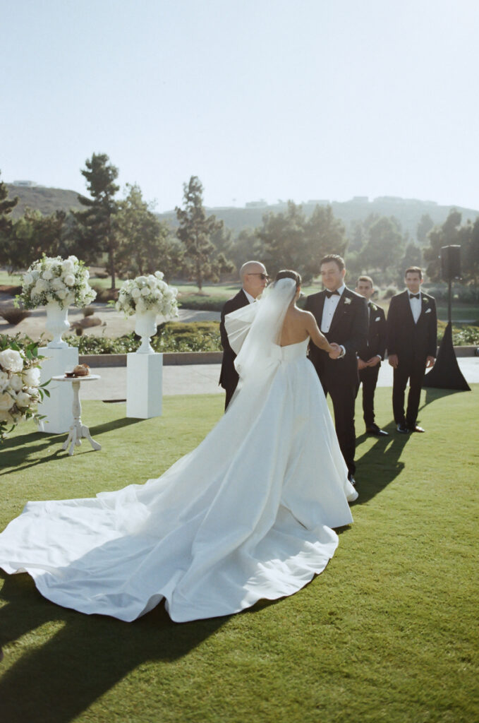 Bride in flowing gown standing at the altar with groomsmen at Del Mar Country Club ceremony.