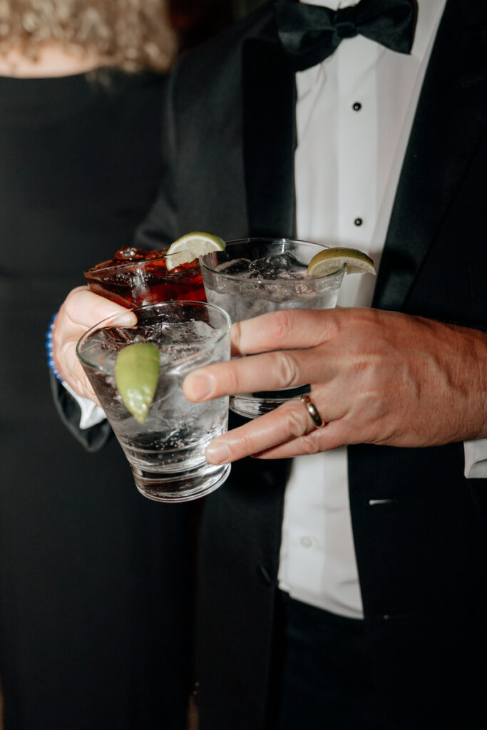 Guest in tuxedo holding cocktails with lime garnish at Del Mar Country Club reception.