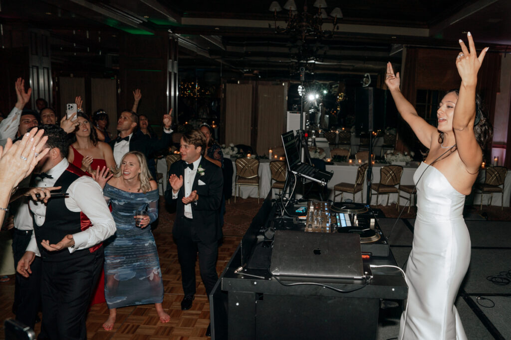 Bride dancing with hands raised on packed dance floor at Del Mar Country Club.