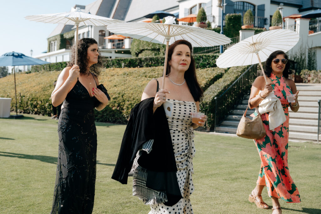 Guests arriving for ceremony with parasols on the lawn at Del Mar Country Club.