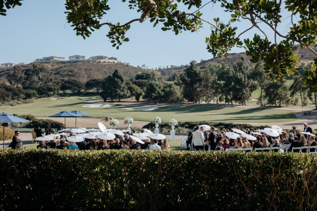 Guests arriving for ceremony with parasols on the lawn at Del Mar Country Club.