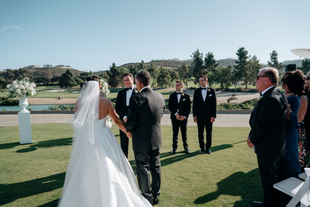 Bride walking up the aisle to meet groom at outdoor ceremony at Del Mar Country Club.
