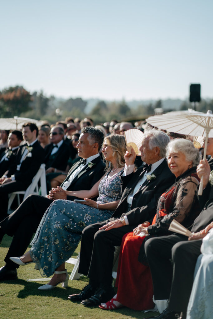Guests seated with parasols watching wedding ceremony at Del Mar Country Club.