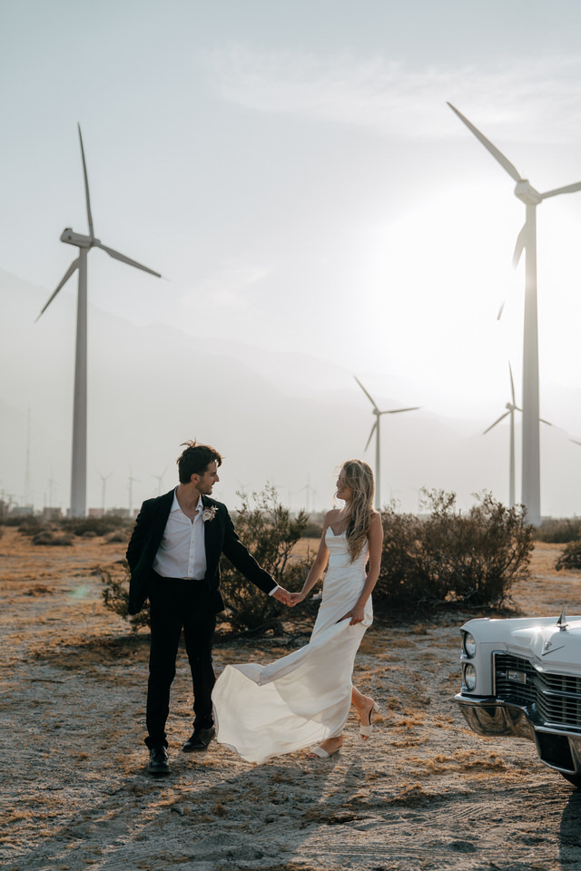 Bride and groom holding hands at sunset in front of Palm Springs windmills