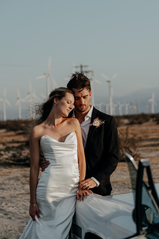 Couple sharing a quiet moment by vintage car with Palm Springs wind farm backdrop