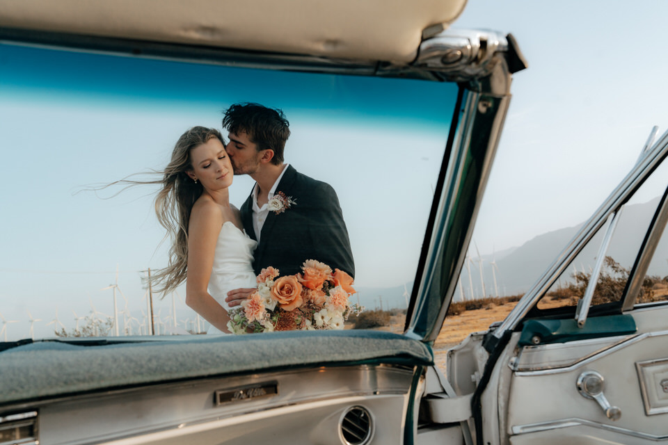 Intimate wedding portrait framed through vintage car window with bouquet in foreground