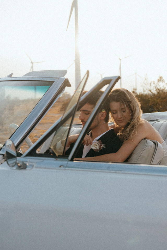 Bride resting on groom’s shoulder during candid wedding photos in classic convertible