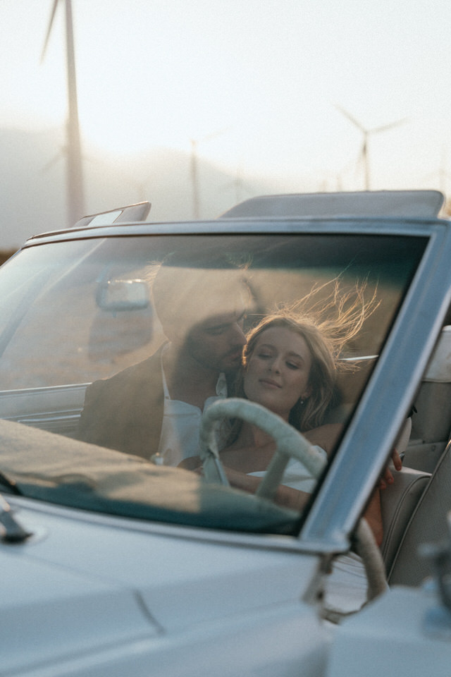 Romantic wedding moment in convertible with golden light shining through windshield