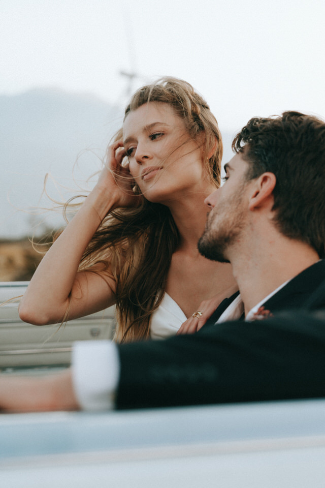 Bride brushing hair back while smiling at groom during relaxed wedding portraits