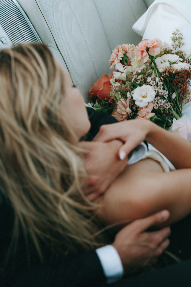 Close-up of bride embracing groom with bouquet of flowers resting in vintage convertible