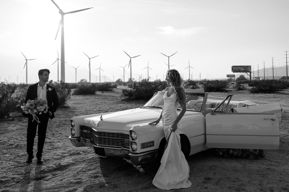 Black and white wedding portrait at Palm Springs windmills with vintage convertible
