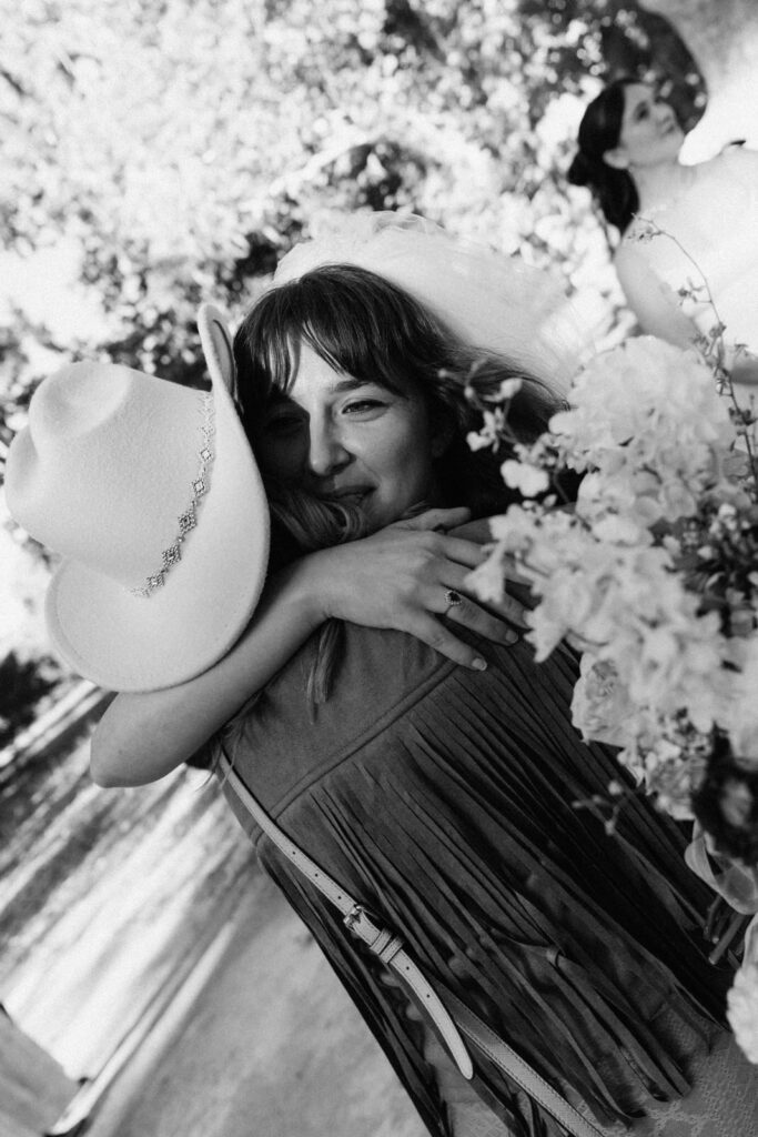 Black and white close up of two guests embracing, one in a cowboy hat
