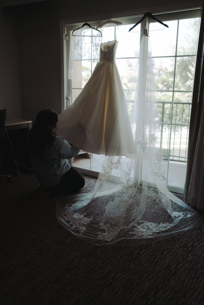 Hillary's wedding gown and veil hanging in a sunlit window before the ceremony