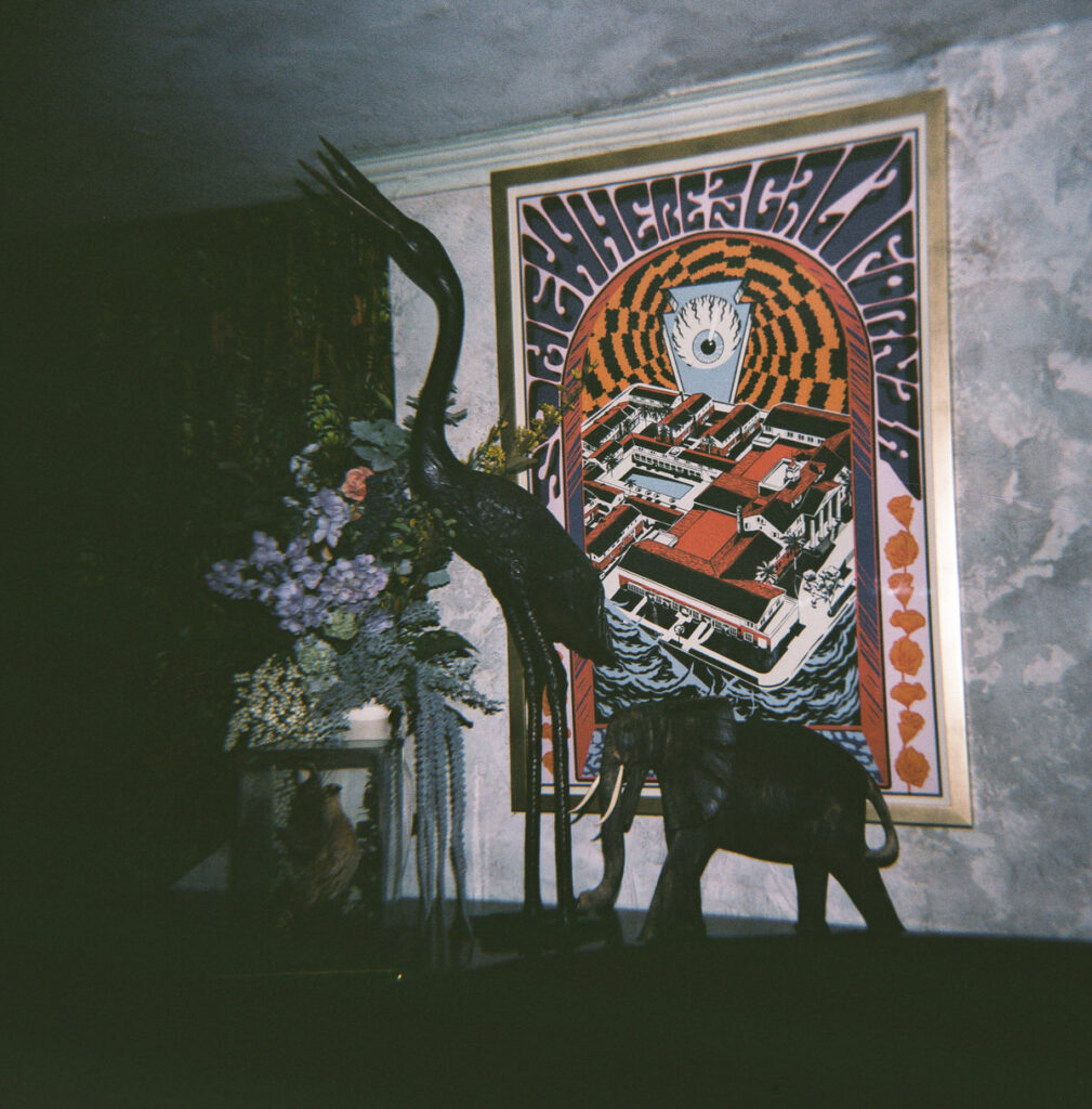 Still life of a bronze crane figure, fresh flowers, and a framed vintage poster on a textured wall