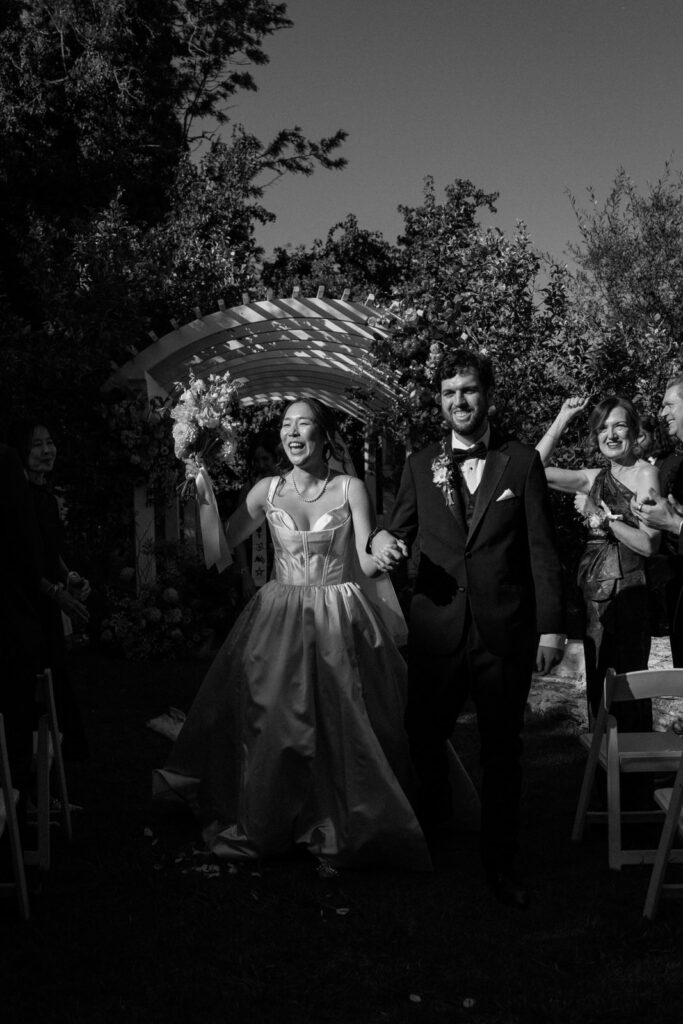 Black and white photo of the bride and groom walking through cheering guests after the ceremony