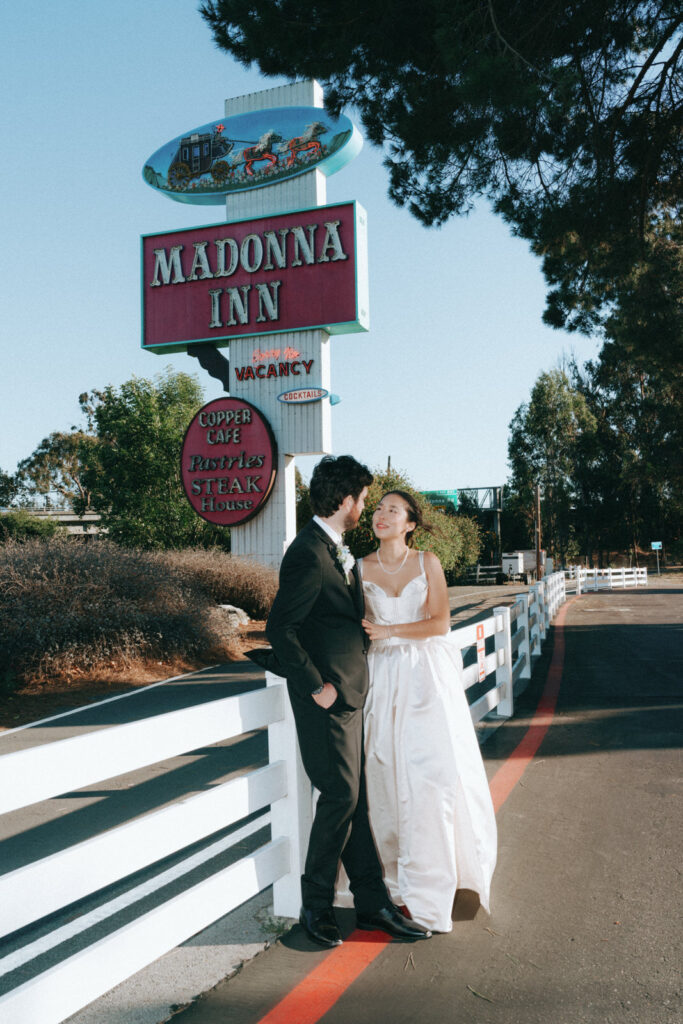 Bride and groom standing beneath the iconic Madonna Inn sign