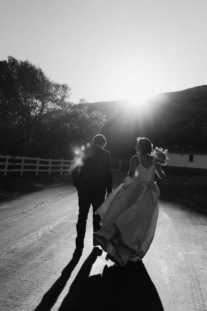 Black and white silhouette of the bride and groom walking together at sunset